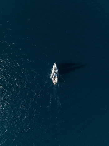 Aerial view of a white sailboat cruising through the deep blue waters of the Mediterranean Sea Plemmirio Sicily Italy. Aerial view of a white sailboat cruising through the deep blue waters of the Mediterranean Sea Plemmirio Sicily Italy.