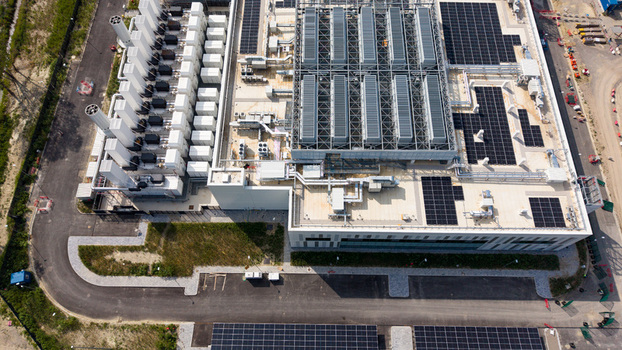 Aerial view of a modern data center campus featuring rooftop solar panels industrial cooling systems and paved access roads in Melegnano Lombardy Italy.