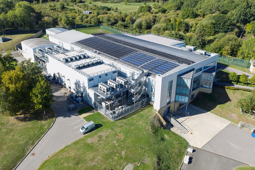 Aerial view of a modern data center facility with rooftop solar panels and cooling units in the United Kingdom.