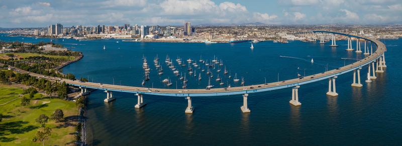 Aerial view of the Coronado Bridge spanning San Diego Bay with sailboats waterfront parkland and the San Diego skyline in Coronado California United States.