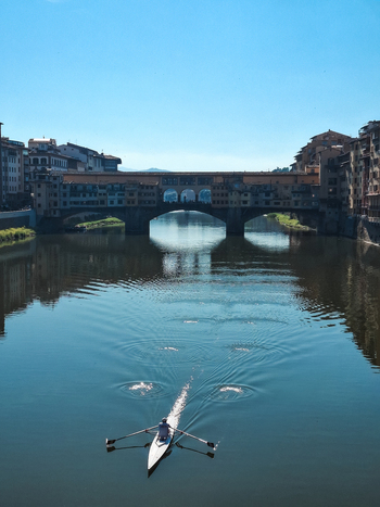 Firenze Italy 26 April 2026 View of Ponte Vecchio with a rower in a scull boat on the Arno River reflecting the historic bridge and buildings under a clear sky.