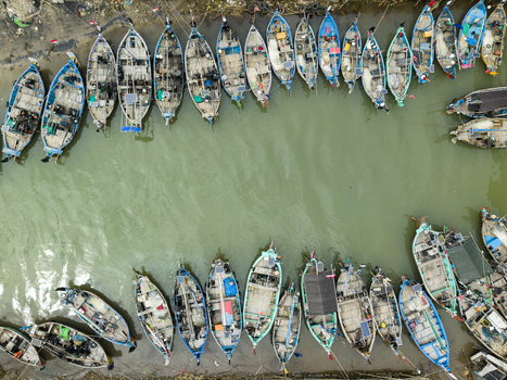 Aerial view of numerous boats tightly packed along the Jepara Floating Fish Market s edge create a textured mosaic on the water Jepara Central Java Indonesia.