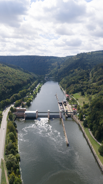 Aerial view of Neckar Staustufe und Schleuse Rockenau on the Neckar river featuring a dam and lock system surrounded by dense forested hills in Eberbach Baden Wurttemberg Germany. Aerial view of Neckar Staustufe und Schleuse Rockenau on the Neckar river featuring a dam and lock system surrounded by dense forested hills in Eberbach Baden Wurttemberg Germany.