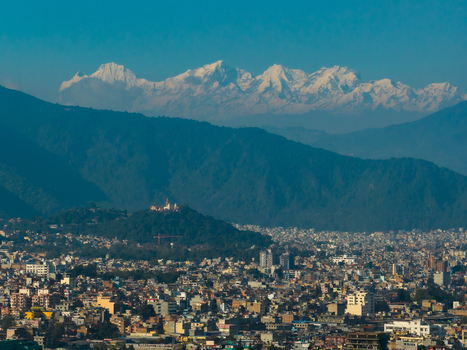 Aerial view of the Swayambhunath Stupa perched on a hill overlooking the dense urban sprawl of Kathmandu with the snow capped Himalayan mountain range in the distance Nepal.