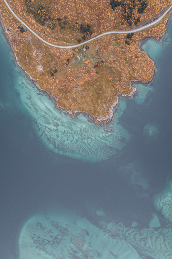 Aerial view of the coastline of Senja featuring turquoise waters rocky shores and a winding road through autumn colored vegetation in Senja Troms Norway.
