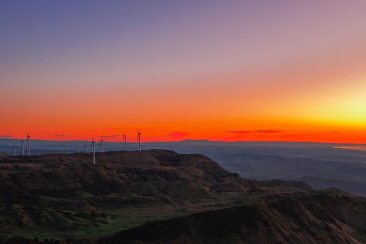 Aerial view of Harapaki Wind Farm with wind turbines on rolling hills during a vibrant sunset in Te Haroto Hawke s Bay Region New Zealand.
