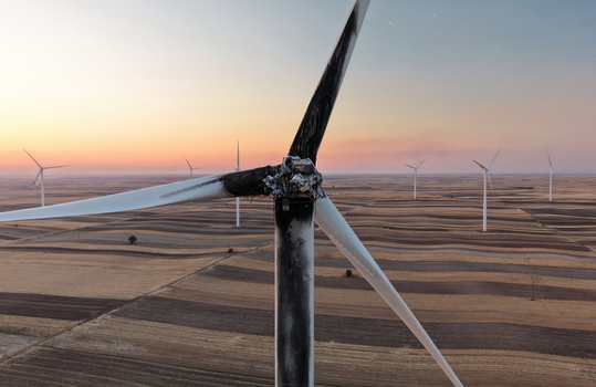 Aerial view of a charred and damaged wind turbine with blackened blades standing in a vast agricultural field during golden hour in Vladimirovac Vojvodina Serbia.