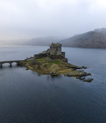 Aerial view of Eilean Donan Castle on its tidal island with the stone bridge and misty hills in the background Dornie Scotland United Kingdom.