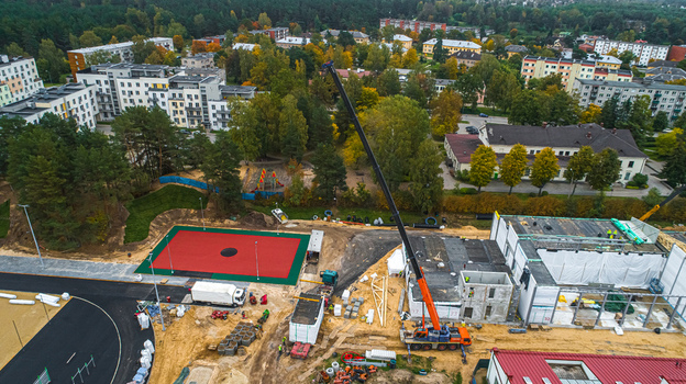 Aerial view of a construction site featuring a tall mobile crane a newly paved red sports court and surrounding residential buildings in Latvia. Aerial view of a construction site featuring a tall mobile crane a newly paved red sports court and surrounding residential buildings in Latvia.