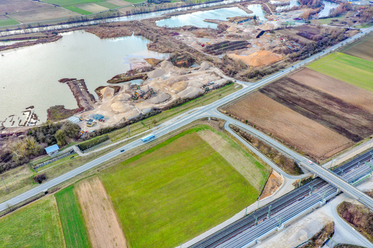 Aerial view of a gravel pit and industrial quarry next to a lake with a road bridge crossing over railway tracks and agricultural fields in Forchheim Bavaria Germany. Aerial view of a gravel pit and industrial quarry next to a lake with a road bridge crossing over railway tracks and agricultural fields in Forchheim Bavaria Germany.