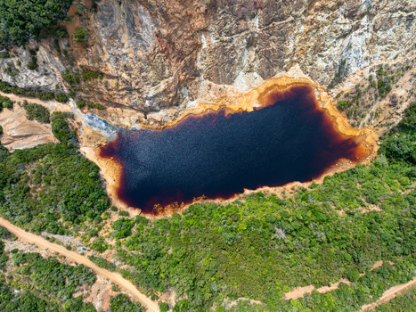 Aerial view of the red water Laghetto delle Conche a former mining quarry surrounded by lush vegetation and rocky cliffs in Rio Marina Toscana Italy.