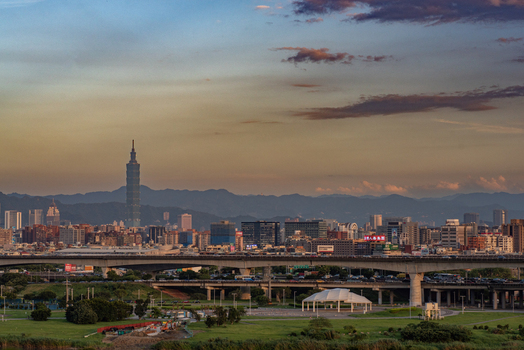 View of Taipei 101 skyscraper rising above the urban skyline with elevated highways green parkland and mountains in the background under a sunset sky Taipei City Taiwan.
