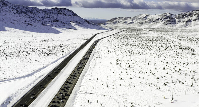 Aerial view of heavy traffic on a highway winding through a snow covered desert landscape with distant mountains under a clear sky in Lancaster CA United States.