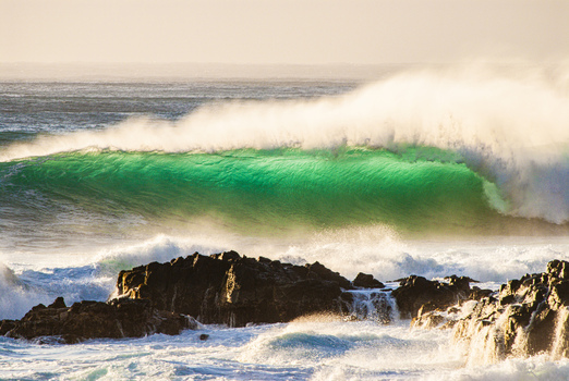 View of a powerful ocean wave breaking over dark volcanic rocks at the North Shore in Haleiwa Hawaii United States.