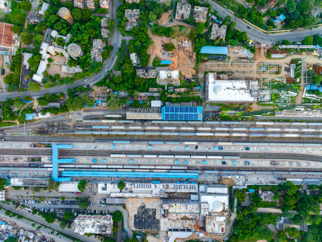 Aerial view of the railway station with multiple tracks platforms and blue roof structures surrounded by urban buildings and lush green trees in Udaipur Rajasthan India. Aerial view of the railway station with multiple tracks platforms and blue roof structures surrounded by urban buildings and lush green trees in Udaipur Rajasthan India.