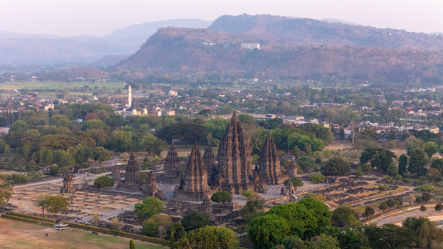 Aerial view of Prambanan Temple featuring stone spires surrounded by lush greenery a village and distant hills in Kecamatan Prambanan Daerah Istimewa Yogya Indonesia.