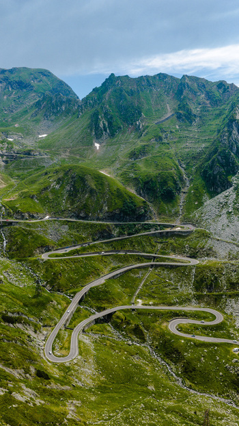 Aerial view of the winding Transfagarasan mountain road snaking through the lush green Fagaras Mountains with rocky slopes and dramatic curves in Curtea de Arges Judetul Arges Romania.