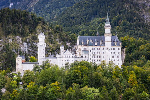 Aerial view of Neuschwanstein Castle a vision of white stone piercing the emerald forest against the backdrop of rugged mountains Neuschwanstein Castle Bayern Germany. Aerial view of Neuschwanstein Castle a vision of white stone piercing the emerald forest against the backdrop of rugged mountains Neuschwanstein Castle Bayern Germany.