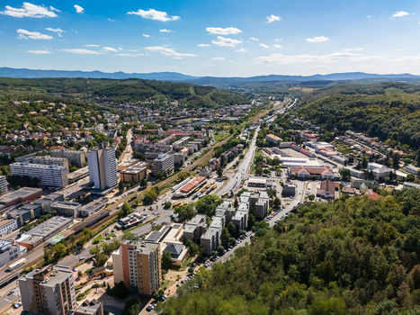 Aerial view of Salgotarjan city center in Hungary with a bus station rail tracks apartment blocks and commercial buildings set between forested hills on a clear summer day. Aerial view of Salgotarjan city center in Hungary with a bus station rail tracks apartment blocks and commercial buildings set between forested hills on a clear summer day.