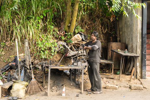 Sri Lanka 20 February 2026 View of a local man working at an outdoor mechanic workshop surrounded by scrap metal parts and dense tropical greenery.