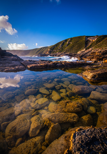 View of Torndirrup National Park featuring clear tide pools with submerged rocks rugged coastal cliffs and crashing waves in Torndirrup Western Australia Australia.
