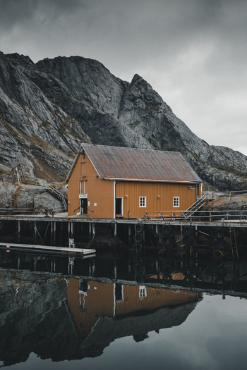 Nusfjord Nordland Norway 07 September 2022 View of the iconic orange rorbu cabin in the historic fishing village of Nusfjord reflected in calm water with dramatic mountains in the background. Nusfjord Nordland Norway 07 September 2022 View of the iconic orange rorbu cabin in the historic fishing village of Nusfjord reflected in calm water with dramatic mountains in the background.