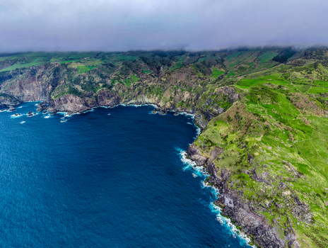 Aerial view of rugged coastline where the dark blue sea crashes against the cliffs creating a stunning contrast with the lush green hillsides Faj&atilde; Grande Azores Portugal.