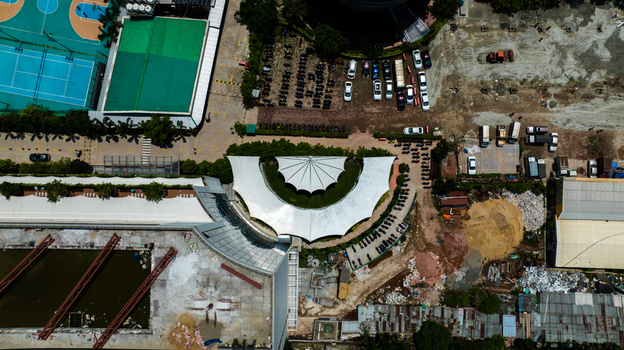 Aerial view of a building complex with a semi circular white canopy adjacent sports courts and parking areas in the urban landscape of Dhaka Dhaka Division Bangladesh. Aerial view of a building complex with a semi circular white canopy adjacent sports courts and parking areas in the urban landscape of Dhaka Dhaka Division Bangladesh.