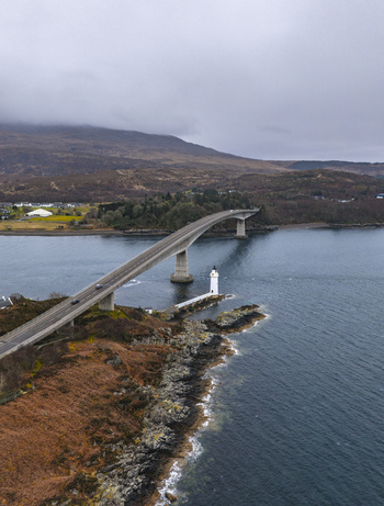 Aerial view of the Skye Bridge spanning the sea with the Kyleakin Lighthouse on the rocky shore under a cloudy sky Isle of Skye Scotland United Kingdom.