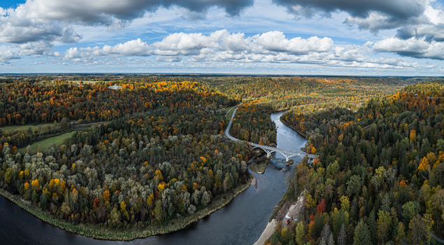 Aerial view of the Gauja River winding through a dense forest with vibrant autumn foliage featuring a bridge crossing the water in Sigulda Sigulda Municipality Latvia. Aerial view of the Gauja River winding through a dense forest with vibrant autumn foliage featuring a bridge crossing the water in Sigulda Sigulda Municipality Latvia.