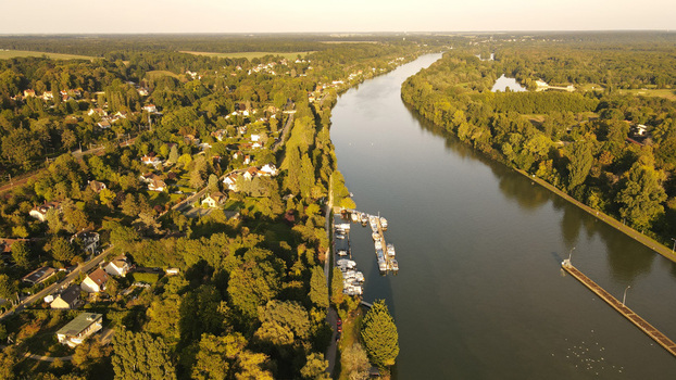 Aerial view of the Seine river flowing past the town of Chartrettes featuring a small marina with docked boats lush green trees and residential houses in Chartrettes Ile de France France. Aerial view of the Seine river flowing past the town of Chartrettes featuring a small marina with docked boats lush green trees and residential houses in Chartrettes Ile de France France.