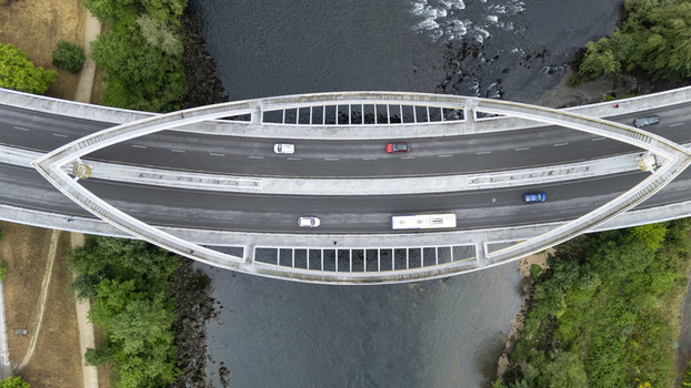 Aerial view of Ponte do Milenio bridge crossing the river with cars and a bus on the asphalt road surrounded by green trees Orense Ourense Spain. Aerial view of Ponte do Milenio bridge crossing the river with cars and a bus on the asphalt road surrounded by green trees Orense Ourense Spain.