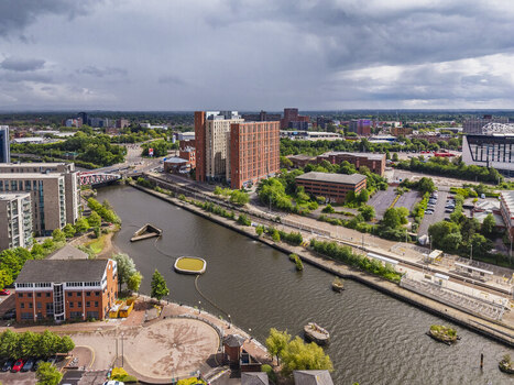 Aerial view of the Manchester Ship Canal flowing through the urban landscape of Stretford with modern buildings and a tram line under a cloudy sky in Stretford England United Kingdom.