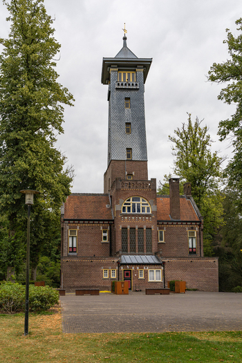 View of De Brandtoren a historic brick fire watch tower surrounded by lush green trees under a cloudy sky in Esbeek Noord Brabant Netherlands.
