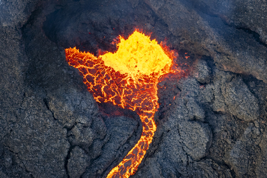 Aerial view of fiery molten lava flows contrasting with the dark rugged landscape of the Reykjanes Peninsula Grindav&iacute;kurb&aelig;r Iceland.