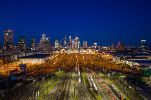 Aerial view of the Hauptbahnhof central station with illuminated tracks and trains against the glowing city skyline at night in Frankfurt am Main Hessen Germany.