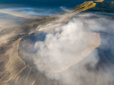 Aerial view of Mount Bromo crater emitting volcanic smoke with rugged slopes and morning light in Tosari East Java Indonesia.