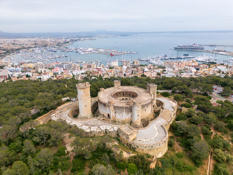 Aerial view of Castillo de Bellver a circular Gothic style fortification surrounded by lush pine forest with the harbor in the background in Palma Illes Balears Spain.