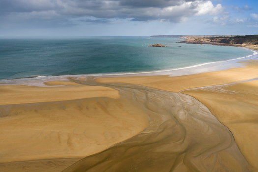 Aerial view of a wide golden sandy beach with a winding river estuary flowing into the turquoise sea under a cloudy sky in Plurien Brittany France. Aerial view of a wide golden sandy beach with a winding river estuary flowing into the turquoise sea under a cloudy sky in Plurien Brittany France.