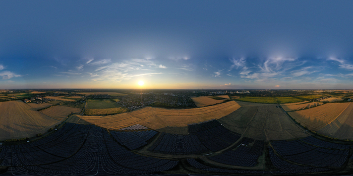 Aerial view of a large solar park at sunset with golden fields and the distant Berlin skyline visible under a clear blue sky in Schonefeld Brandenburg Germany. 360 degree.