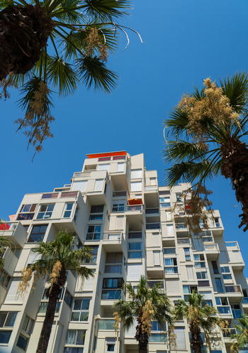 La Grande Motte Occitanie France 17 July 2026 View of the iconic stepped modernist architecture of apartment buildings framed by lush palm trees under a clear blue sky.