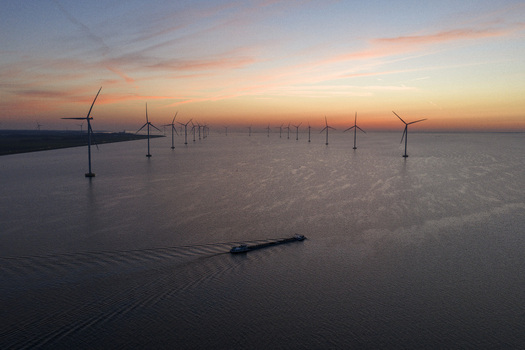Aerial view of IJsselmeer wind farm with offshore turbines and a cargo ship on the water at sunset in Netherlands.