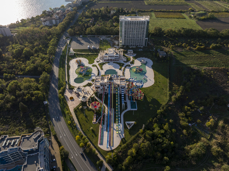 Aerial view of a vibrant water park featuring multiple colorful slides swimming pools and a large hotel complex situated near a coastal road and lush green fields in Bulgaria. Aerial view of a vibrant water park featuring multiple colorful slides swimming pools and a large hotel complex situated near a coastal road and lush green fields in Bulgaria.