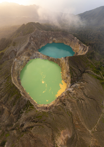 Aerial view of Kelimutu National Park with its iconic turquoise and green volcanic crater lakes surrounded by rugged mountain terrain Detusoko East Nusa Tenggara Indonesia.