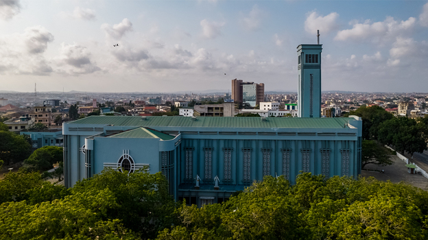 Aerial view of Holy Spirit Cathedral with its distinctive blue facade and green roof surrounded by lush trees and the urban skyline of Accra Greater Accra Region Ghana. Aerial view of Holy Spirit Cathedral with its distinctive blue facade and green roof surrounded by lush trees and the urban skyline of Accra Greater Accra Region Ghana.