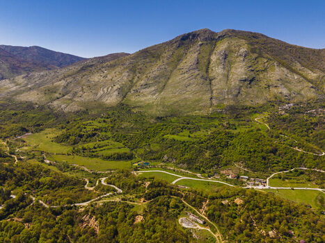 Aerial view of the mountainous landscape of Muzine featuring winding roads lush green vegetation and rocky slopes under a clear blue sky in Muzina Qarku i Vlores Albania. Aerial view of the mountainous landscape of Muzine featuring winding roads lush green vegetation and rocky slopes under a clear blue sky in Muzina Qarku i Vlores Albania.