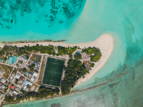 Aerial view of a vibrant football field nestled amidst the tropical greens and white sands bordered by the turquoise sea Vashafaru Island Maldives.