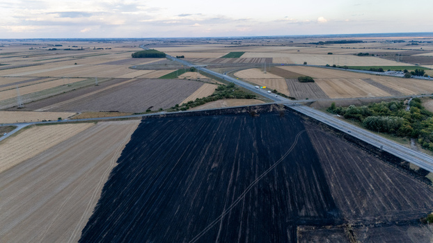 Aerial view of a large burnt agricultural field adjacent to a highway and surrounding cultivated farmland in Sremska Mitrovica Vojvodina Serbia.