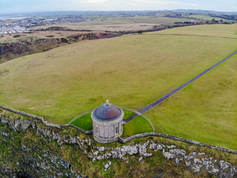 Aerial view of Mussenden Temple perched on a cliff edge with green fields and stone walls in Coleraine Northern Ireland United Kingdom. Aerial view of Mussenden Temple perched on a cliff edge with green fields and stone walls in Coleraine Northern Ireland United Kingdom.