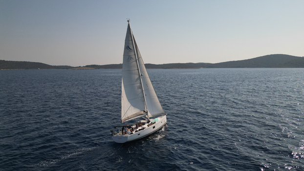 Split Dalmatia County Croatia 22 August 2023 Aerial view of a white sailboat navigating the deep blue waters of the Adriatic Sea near the hilly coastline of Hvar. Split Dalmatia County Croatia 22 August 2023 Aerial view of a white sailboat navigating the deep blue waters of the Adriatic Sea near the hilly coastline of Hvar.